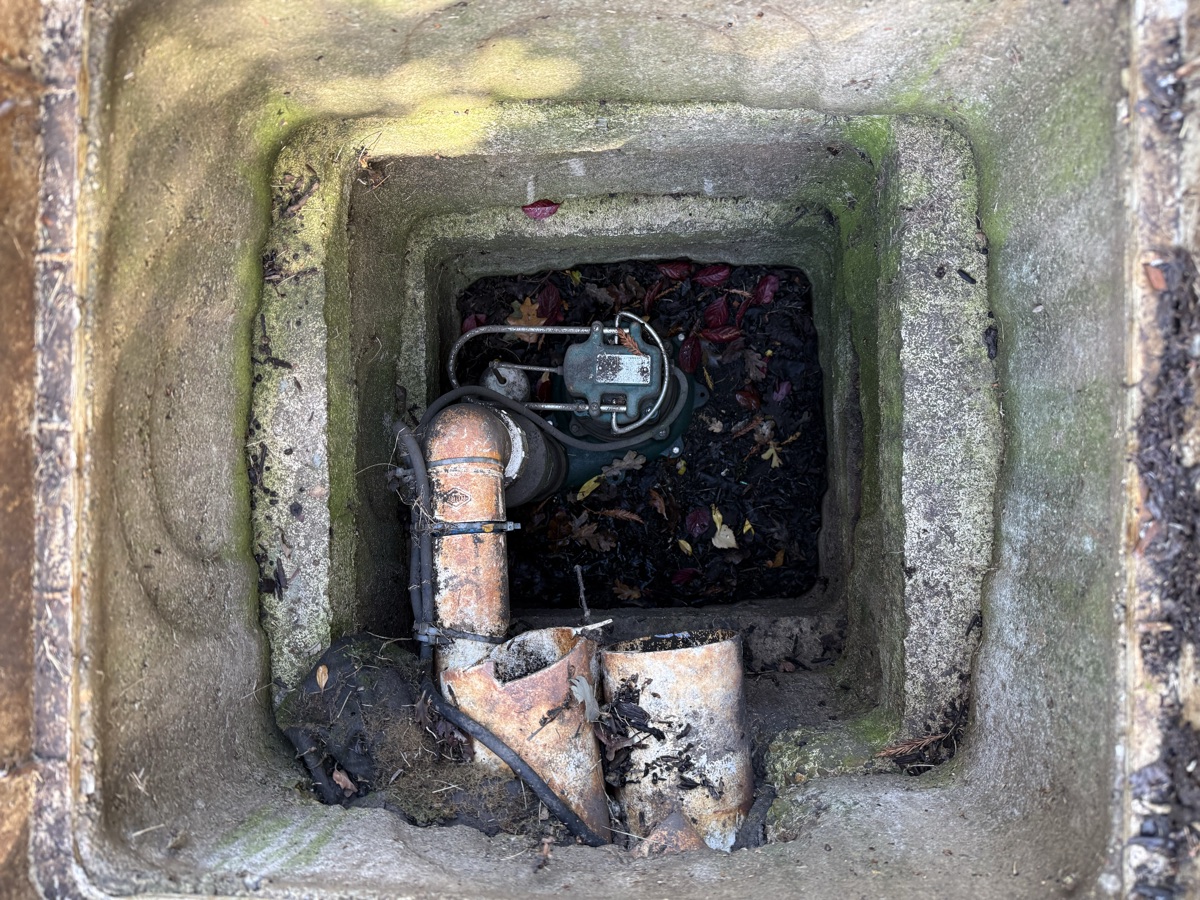 Looking down into the rear concrete sump pit at the inoperative pump, its float and the discharge pipe
